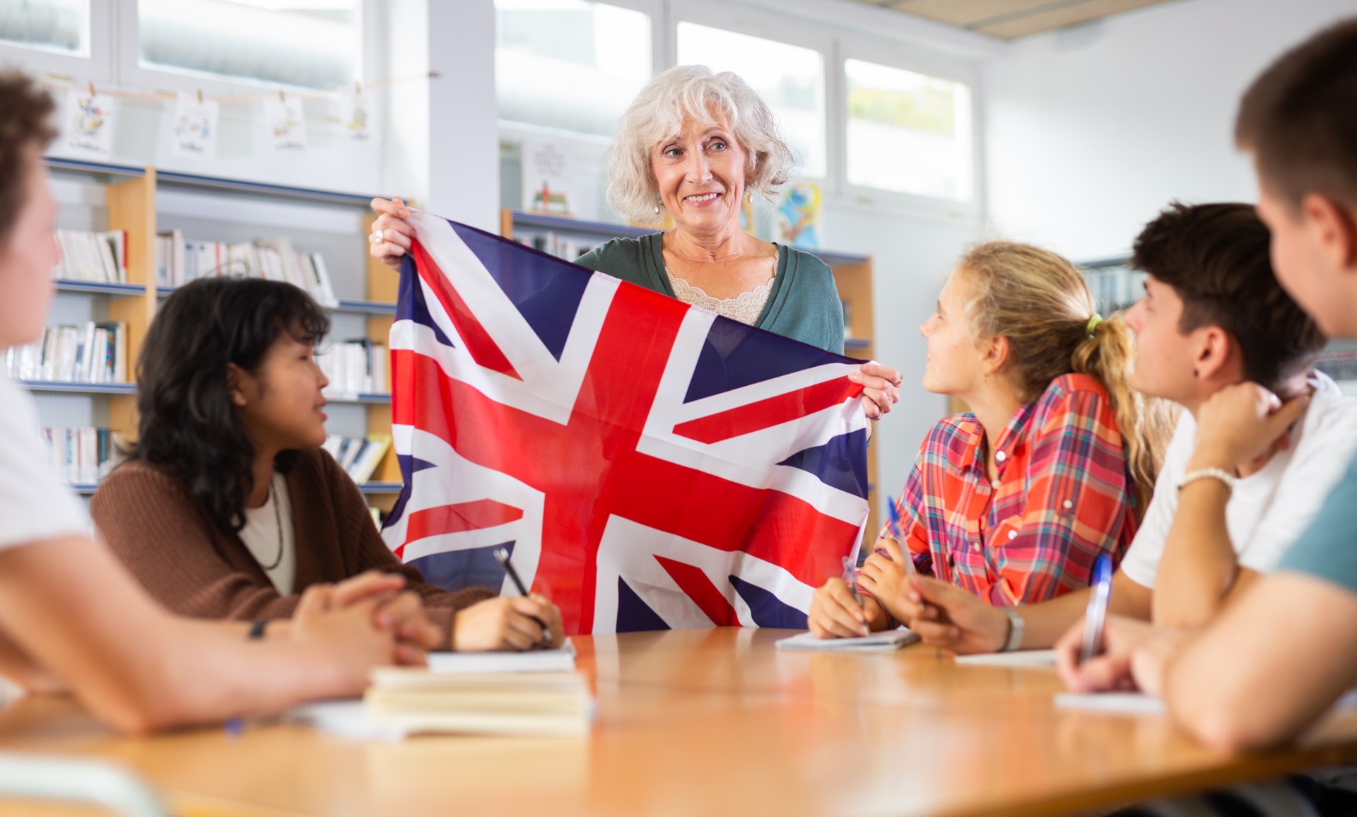 Adult female teacher discussing with children about national flag of the Great Britain at Geography lesson in library