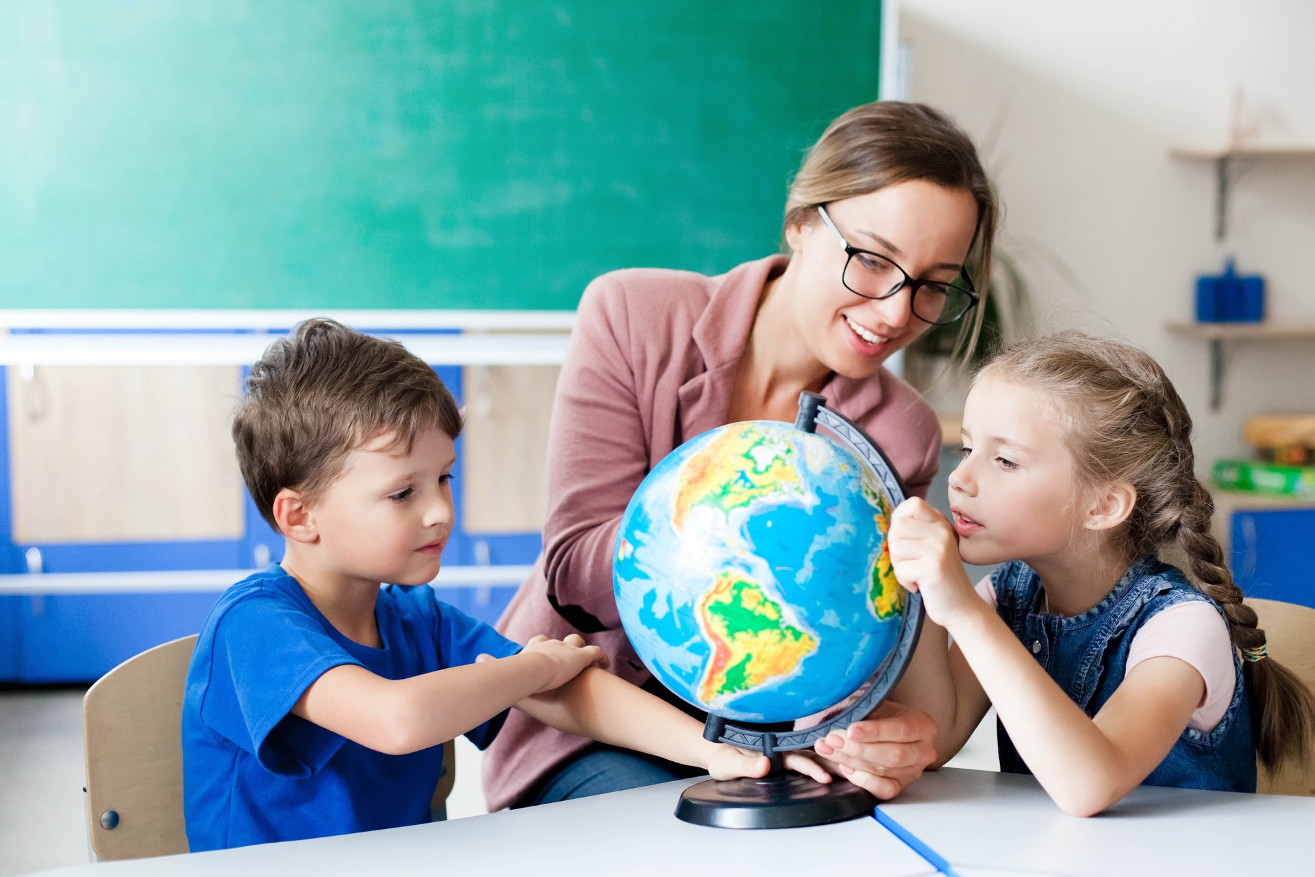 Teacher and kids study the globe in classroom at elementary school. Lesson for children in classroom.