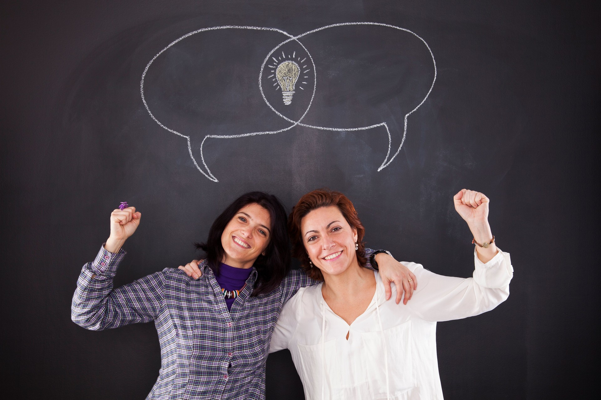 Two women stand side by side, their faces animated with inspiration as they collectively develop an idea